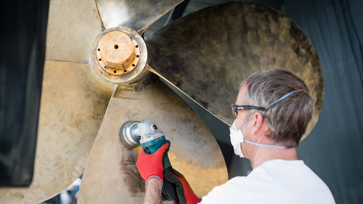Man in protective face mask polishing a boat propeller